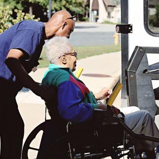 A caregiver assisting an elderly person in a wheelchair outdoors.