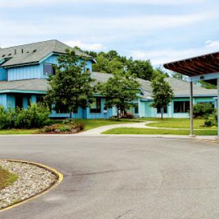 A modern blue building surrounded by greenery, featuring a curved driveway.