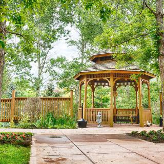 A serene garden featuring a wooden gazebo surrounded by lush greenery.