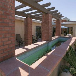 A patio area with a pergola supported by brick columns and an adjacent water feature on a sunny day.