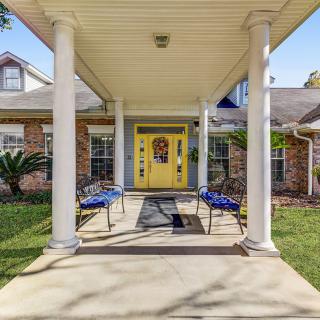 A welcoming entrance to a house featuring a yellow door, flanked by two benches and supported by white columns.