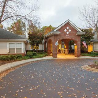 A brick building entrance with a circular driveway surrounded by autumn trees.