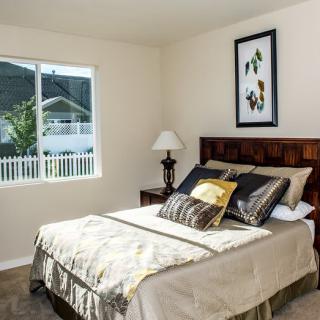 A cozy bedroom with a neatly made bed, decorative pillows, and a window letting in natural light.