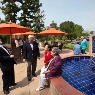 A group of people socializing near a fountain on a sunny day with umbrellas providing shade.