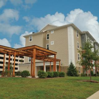 A modern residential building surrounded by landscaped greenery under a blue sky.