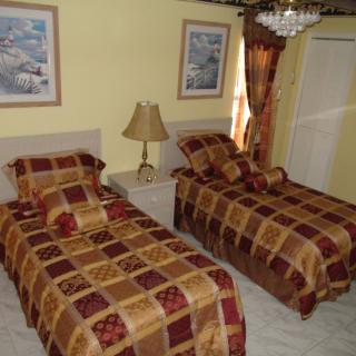 A cozy bedroom with twin beds featuring patterned covers, decorated with framed pictures and a chandelier.