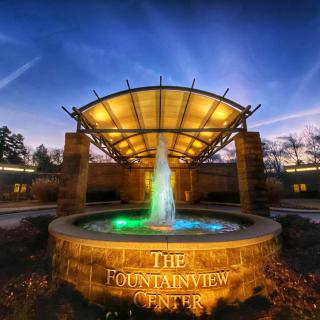 An illuminated fountain at night in front of a building with modern architecture.