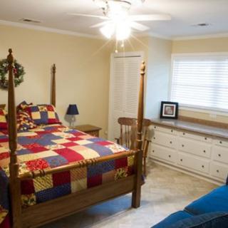 A cozy bedroom with a quilt-covered bed, a white dresser, and a chair near the window.