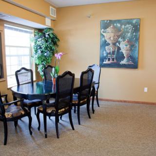 A dining room with a black table and chairs, an artwork on the wall, and a window providing natural light.
