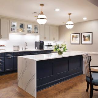 A modern kitchen with a marble island, dark cabinetry, and pendant lighting.