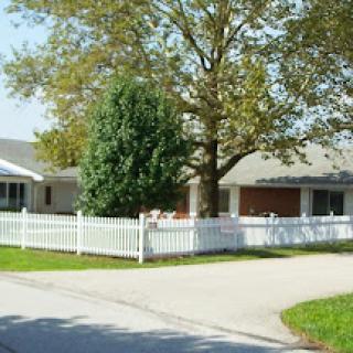 A charming suburban house with a white picket fence and a large tree in the front yard.