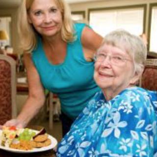 A caregiver assists an elderly woman with her meal in a nursing home setting.