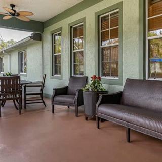 A cozy patio area with comfortable seating and a table, surrounded by green walls and windows.