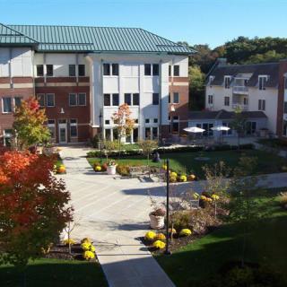A scenic view of a university campus courtyard during autumn, with trees showcasing fall colors and adjacent buildings under a clear blue sky.