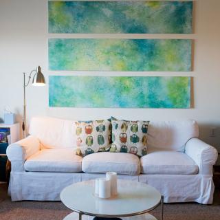 A cozy living room featuring a white sofa with colorful cushions, plemented by abstract artwork on the wall.