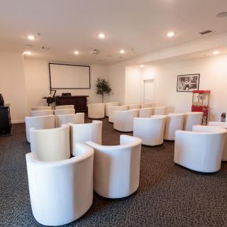A modern conference room with a projector screen and white armchairs arranged for a presentation.
