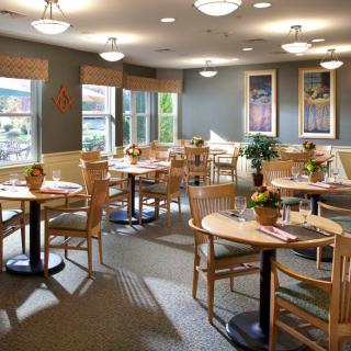 A cozy restaurant interior with wooden tables and chairs, decorated with plants and art on the walls.
