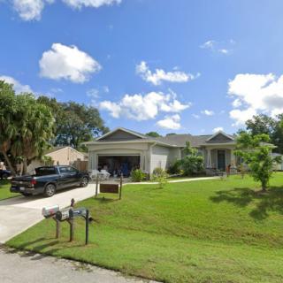A suburban house with a well-maintained yard, driveway, and parked car under a clear blue sky.