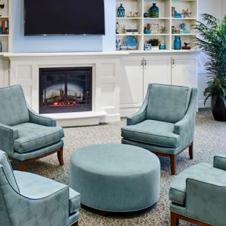 A cozy living room with teal chairs, a round ottoman, and a fireplace surrounded by built-in bookshelves.