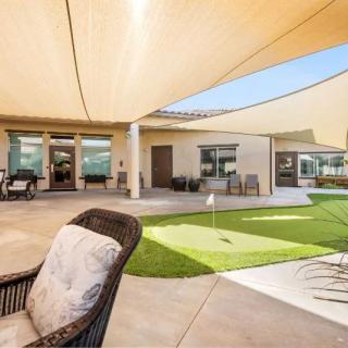 A modern backyard with shade sails, outdoor seating, and a golf putting green on a sunny day.