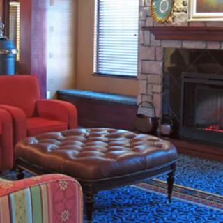A cozy living room with a red armchair, leather ottoman, and a fireplace.