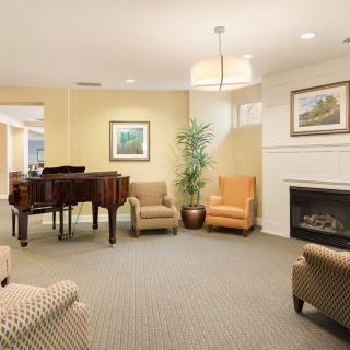 A cozy living room featuring a grand piano, comfortable seating, a fireplace, and artwork on the walls.