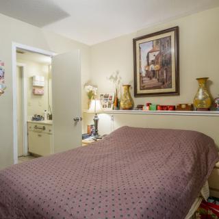 A cozy bedroom with a neatly made bed, decorative vases, and a painting on the wall.