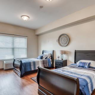 A neatly arranged bedroom with two beds, a nightstand, lamps, and a large window.