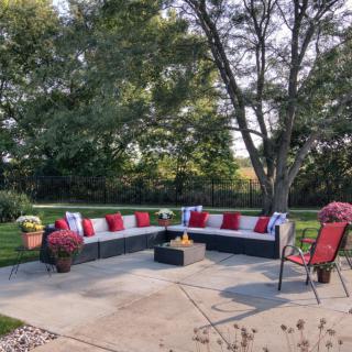 A cozy patio area with cushioned seating and a fire pit surrounded by lush greenery.
