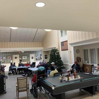 A group of seniors gathered in a community room with a Christmas tree and pool table.