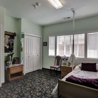 A cozy bedroom with a single bed, carpeted floor, and ample natural light from the windows.