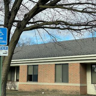 A building with a handicap parking sign in front, accompanied by a bare tree against a cloudy sky.