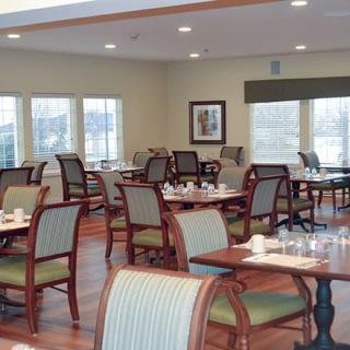 An empty dining room with neatly arranged tables and chairs, illuminated by overhead lights.