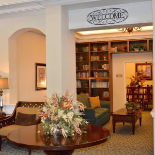 A cozy lounge area with comfortable seating, a bookshelf, and decorative flowers on a table.