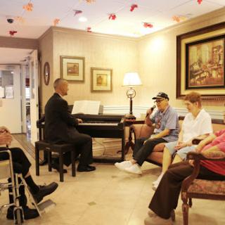 A performer plays the piano for a group of elderly residents in a cozy common area, fostering community and enjoyment through music.