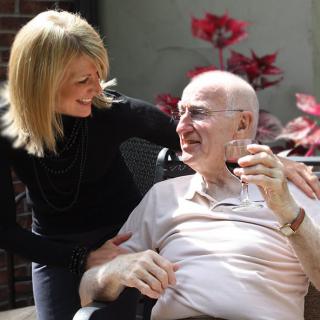 A caregiver shares a moment of joy with an elderly man outdoors.
