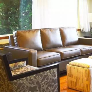 A cozy living room with a leather sofa, patterned armchair, and ottoman next to a large window.