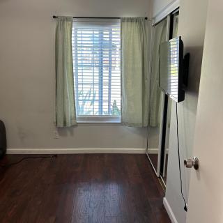 A minimalist room with a window, curtains, and a wall-mounted television.