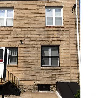 A brick house with two windows, a door, and a small set of stairs leading to the entrance.