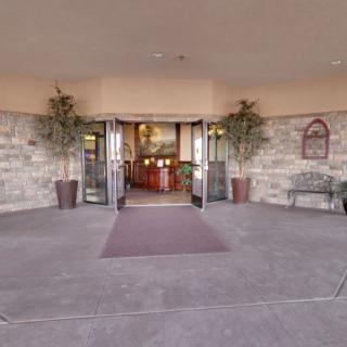 The image shows the entrance of a building with large glass doors, stone walls, and decorative plants.