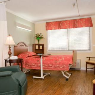 A well-equipped hospital room featuring a comfortable bed, seating area, and medical equipment stand.