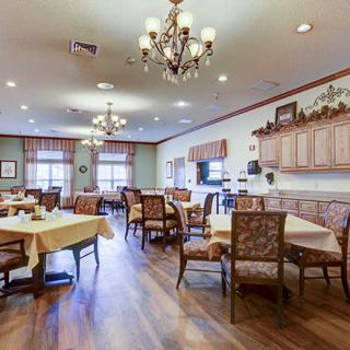 A cozy dining area with chandeliers, wooden flooring, and elegantly decorated tables and chairs.