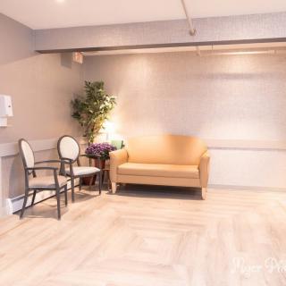 A minimalist waiting room with a sofa, chairs, and a potted plant, featuring light wood flooring and warm lighting.