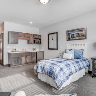 A modern bedroom with a single bed featuring blue plaid bedding, a kitchenette in the corner, and stylish wall art.