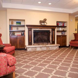 A cozy living room with a fireplace, featuring red armchairs and a patterned carpet.