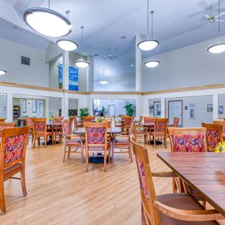 A spacious dining hall with wooden tables and chairs, illuminated by decorative lighting fixtures.