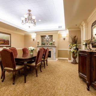 An elegantly decorated dining room featuring a chandelier, long dining table, cushioned chairs, and a warm fireplace.