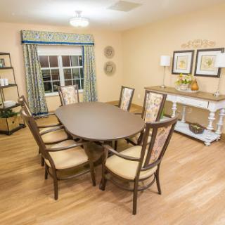 A cozy dining room featuring an oval table and upholstered chairs, complemented by warm lighting and soft color tones.
