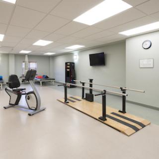 A physical therapy room equipped with a recumbent bike and parallel bars for rehabilitation exercises.