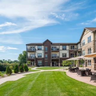 A modern apartment building with a well-maintained lawn and outdoor seating area under a bright blue sky.